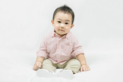 Portrait of cute baby boy sitting against white background