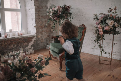 Full length of boy sitting by flower vase on floor