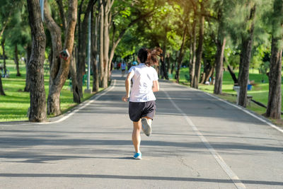 Rear view of woman running on road against trees