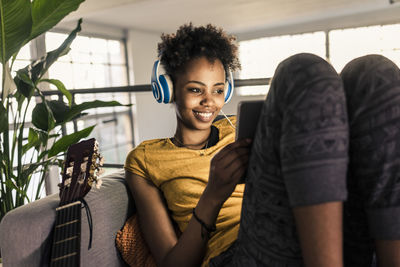 Smiling young woman on couch with headphones using tablet