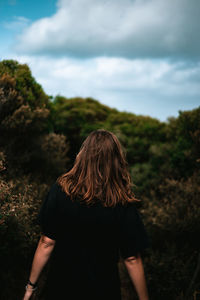 Rear view of woman walking in forest against sky