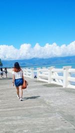 Rear view of woman walking on pier over sea against sky