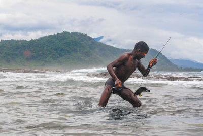 Full length of shirtless man holding sea against sky