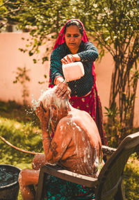 Daughter bathing her old mother in yard