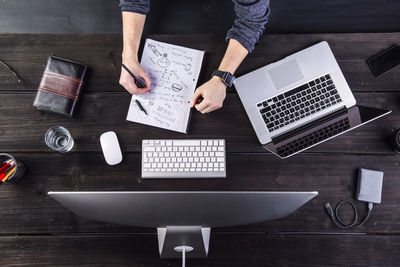 Man working at desk with computer and laptop taking notes on sheet of paper