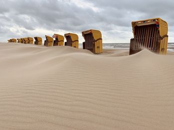 Hooded beach chairs on sand against sky