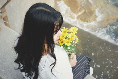 Rear view of woman holding flowers while sitting outdoors