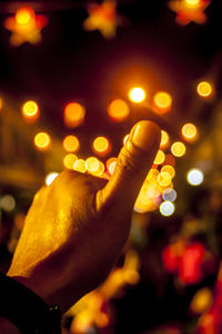 Close-up of human hand against illuminated lights at night