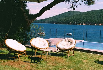Chairs and table by swimming pool against lake