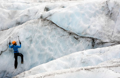 Woman climbing ice wall on sólheimajökull glacier in iceland