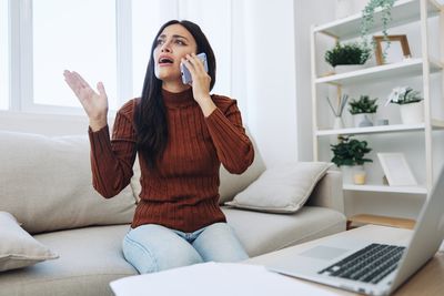 Young woman using phone while sitting on sofa at home