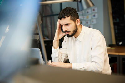 Tensed businessman looking at laptop while sitting in creative office