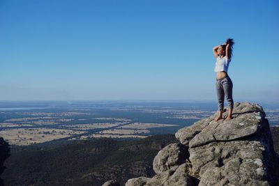 Young woman standing on rock formation against clear blue sky
