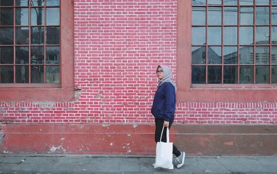 Full length side view of woman standing against brick wall