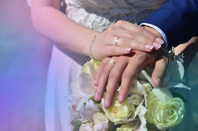 Midsection of bride and groom holding bouquet