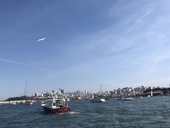 Sailboats in sea by buildings against sky