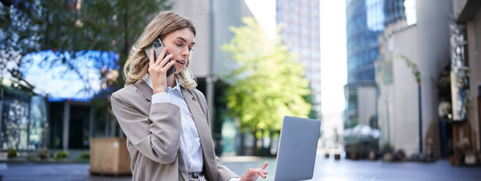 Portrait of young woman using mobile phone in city