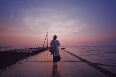 Rear view of woman standing on pier in sea against sky