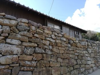 Low angle view of stone wall by building against sky