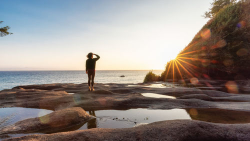 Woman standing on rocks at beach against sky during sunset