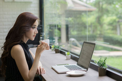 Businesswoman drinking coffee while using laptop at desk in office