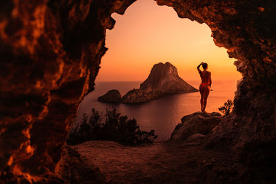 Man standing on rock by sea against sky