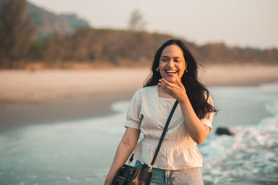 Happy young woman standing on the beach against the sea and laughing 