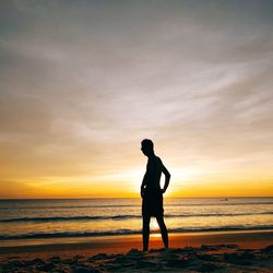 Silhouette boy standing on beach against sky during sunset