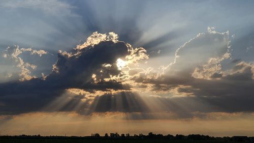 Low angle view of sunlight streaming through clouds