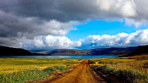 Road passing through field against cloudy sky