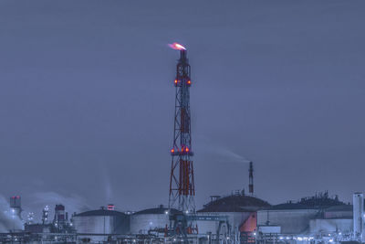 Factory in city against sky at dusk