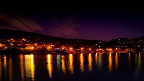Illuminated city by river against sky at night