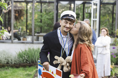 Woman kissing son while standing at back yard during summer party