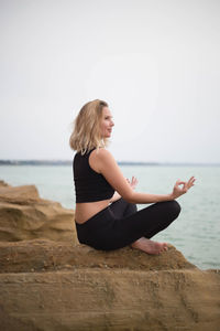 Young woman sitting on shore at beach against sky