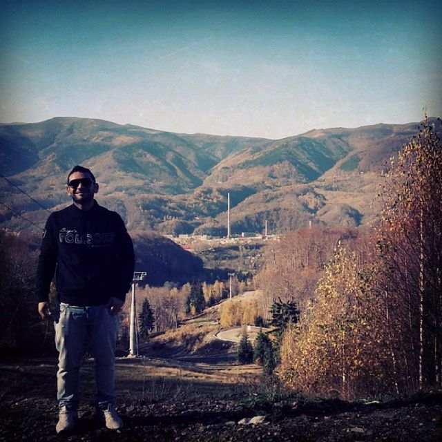 mountain, lifestyles, leisure activity, standing, casual clothing, young adult, landscape, tranquil scene, mountain range, full length, tranquility, young men, scenics, clear sky, person, beauty in nature, three quarter length