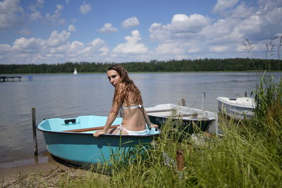 Portrait of young woman in boat on lake against sky