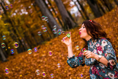 Mid adult woman blowing bubbles in forest during autumn