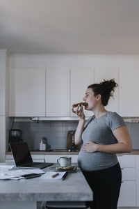 Pregnant woman working from home while eating breakfast