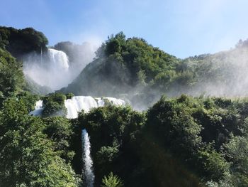 Scenic view of waterfall in forest against sky