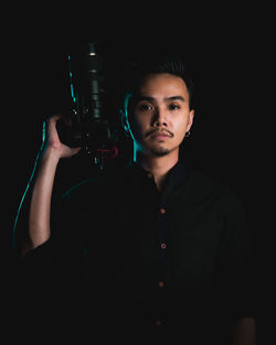 Portrait of young man standing against black background