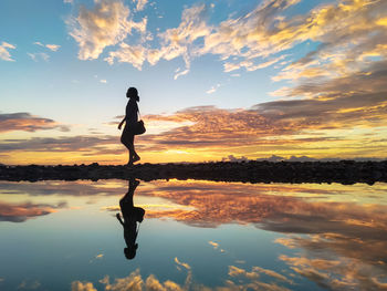 Silhouette woman standing on shore against sky during sunset