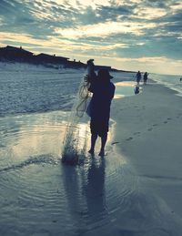 Man walking on beach against sky during sunset