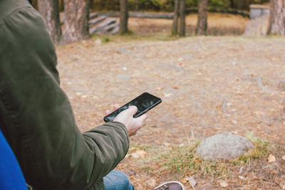 Low section of man using mobile phone on land