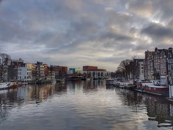 Boats moored at harbor in city against sky