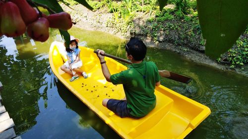 A girl with a father sitting in a yellow boat rowing in an orchard canal