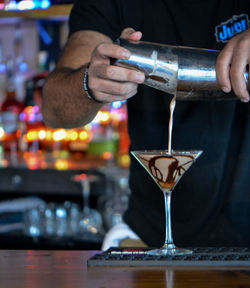 Midsection of man pouring drink in glass on table