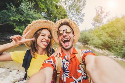 Portrait of excited man and woman wearing hat against trees