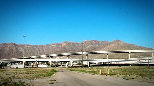 Road leading towards mountains against clear blue sky