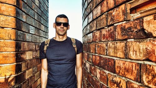 Portrait of young man standing between brick walls