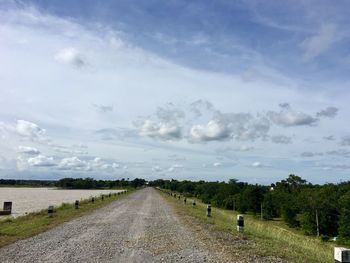 Empty road amidst field against sky